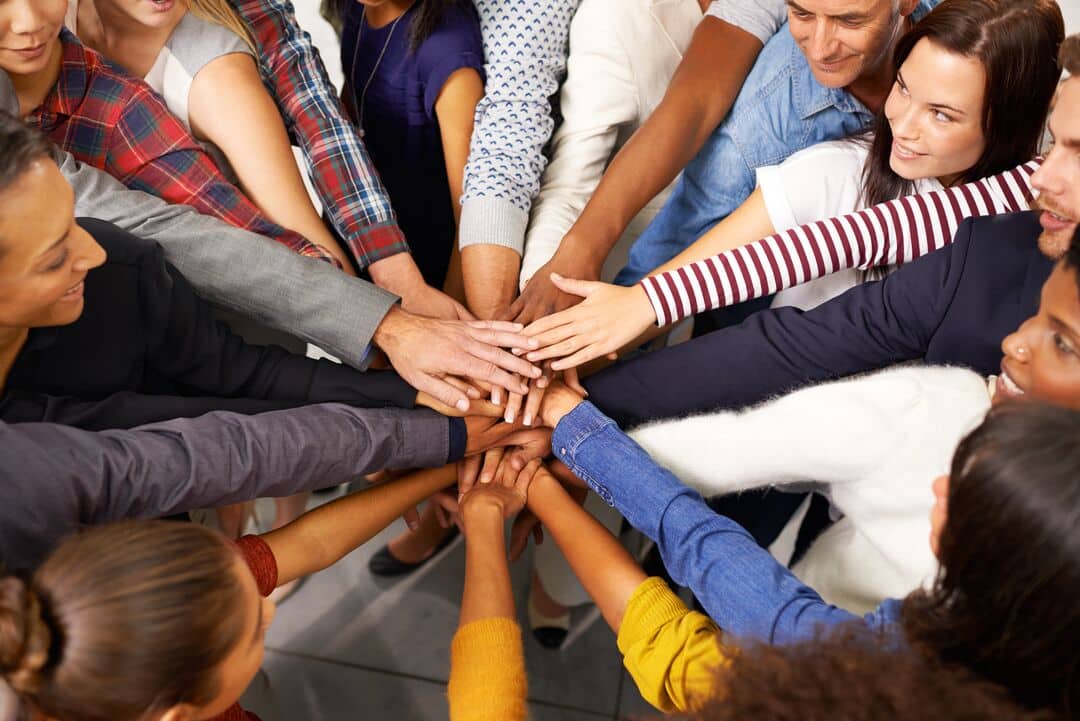 A group of people stand in a circle with their hands meeting in the middle.