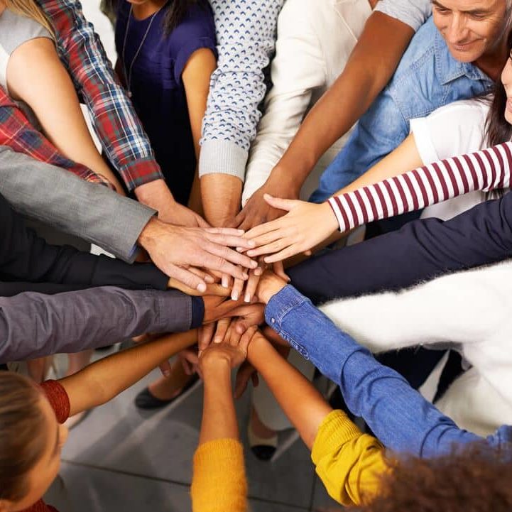 A group of people stand in a circle with their hands meeting in the middle.